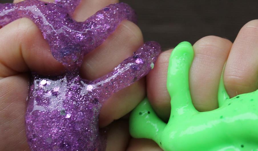 two children's hands holding purple and green slime
