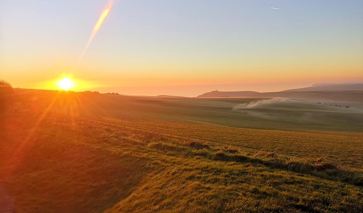 view from the Beachy Head Story towards Belle Tout with sun setting on left of image