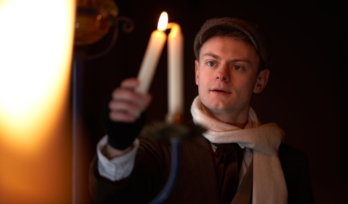 A character from A Christmas Carol holds a candle