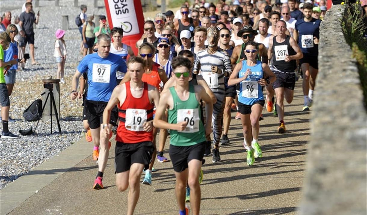 Group of runners in a race running on a path alongside a pebble beach