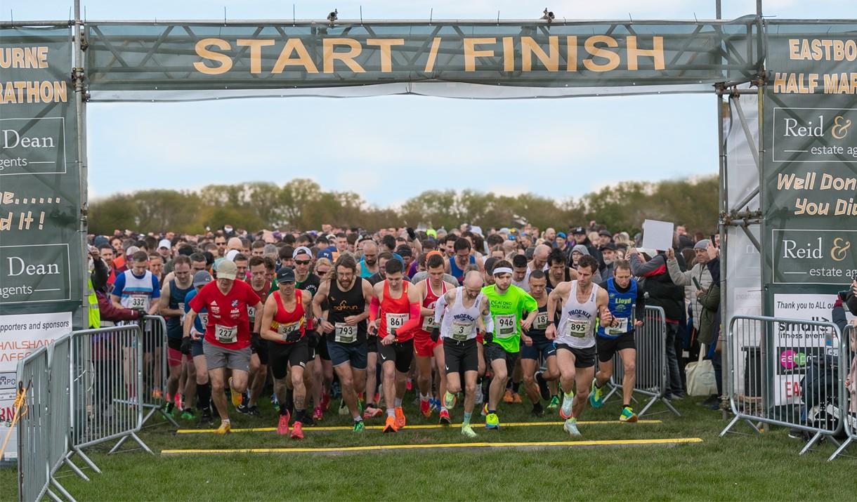 Group of runners about to start a race in a park, running through a green start/finish gantry