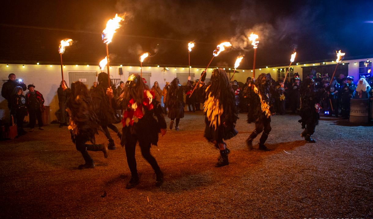Morris dancers dance with fire in a historic courtyard, after dark