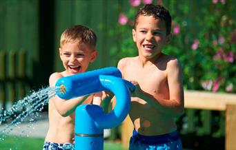 Two children in swimming costumes pointing a water pistol