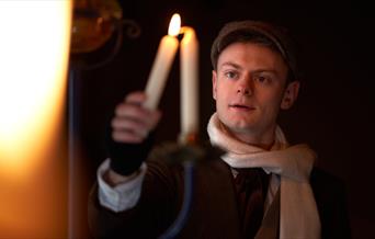 A character from A Christmas Carol holds a candle