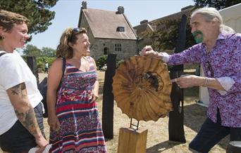 woodworker shows his craft to two smiling onlookers
