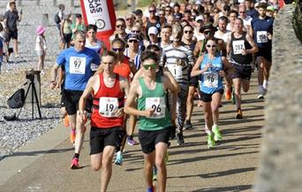 Group of runners in a race running on a path alongside a pebble beach