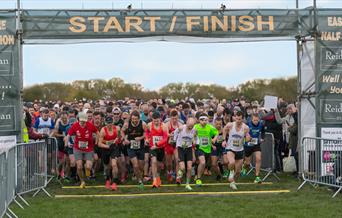 Group of runners about to start a race in a park, running through a green start/finish gantry