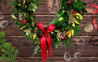 A festive wreath on a table with red bows and scissors