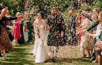 Bride and groom walk down the aisle while guests throw confetti at them