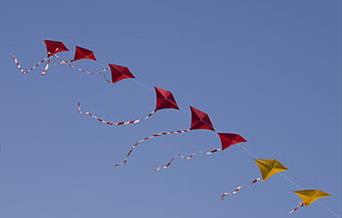 A diagonal line of red and yellow diamond shaped kites in a blue sky
