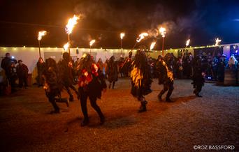 Morris dancers dance with fire in a historic courtyard, after dark