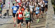 Group of runners in a race running on a path alongside a pebble beach