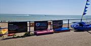 Bourne to Kayak banners fixed to blue railings with the beach, sea and blue sky in the background