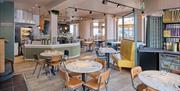 Empty interior of Pizza Express restaurant, with circular tables, pastel colours on the seating and big windows