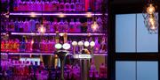 Close up shot of the East Beach Hotel Bar with pink backlit shelves of alcohol in the background and beer pumps in the foreground