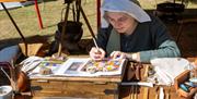 A woman dressed in medieval style clothing demonstrates a painting craft