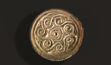 Shiny gold saucer brooch from Saxon Eastbourne with spiral decoration around edge