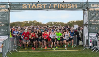 Group of runners about to start a race in a park, running through a green start/finish gantry