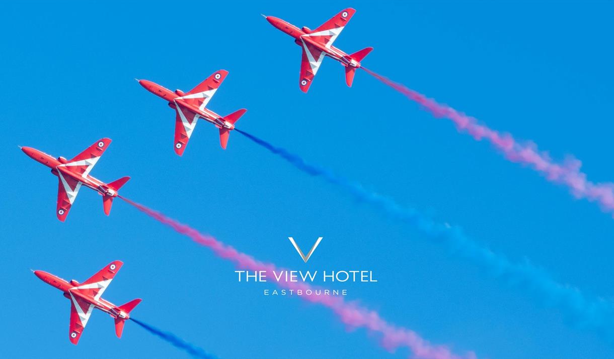 Four red arrows jets flying alongside each other on a clear blue sky with red and blue vapour trails following the jets