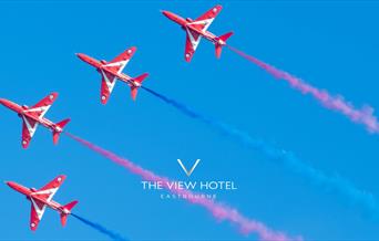 Four red arrows jets flying alongside each other on a clear blue sky with red and blue vapour trails following the jets