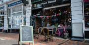 The exterior of The Good Grub with outside tables, a pink bicycle and multi coloured bunting in the window