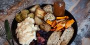A close up of a plate of vegan roast dinner with stuffing, potatoes, carrots, sprouts, gravy and a meat alternative