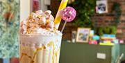 Close up of a milkshake topped with whipped cream, marshmallows, a white and yellow striped straw and a mini pink disco ball.