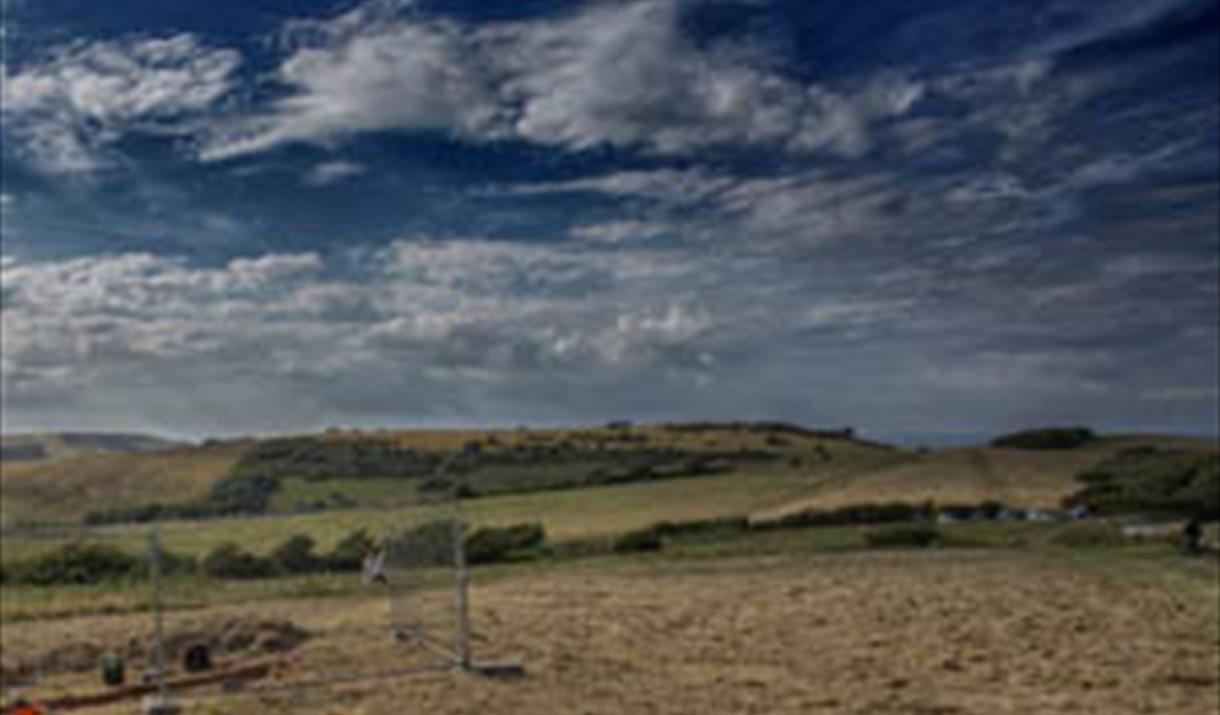 View at Butts Brow with very blue sky and rolling green fields showing archaeological excavation in bottom left corner