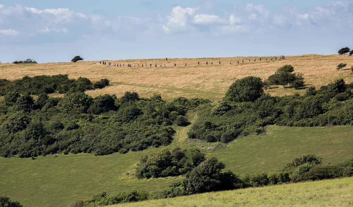 Group of people standing in a big circle on a hill top marking out the ditch of the Neolithic causewayed enclosure at Combe Hill