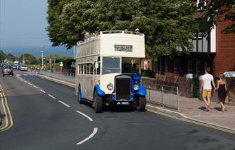 White and blue classic open top bus on the road with the sea in the background