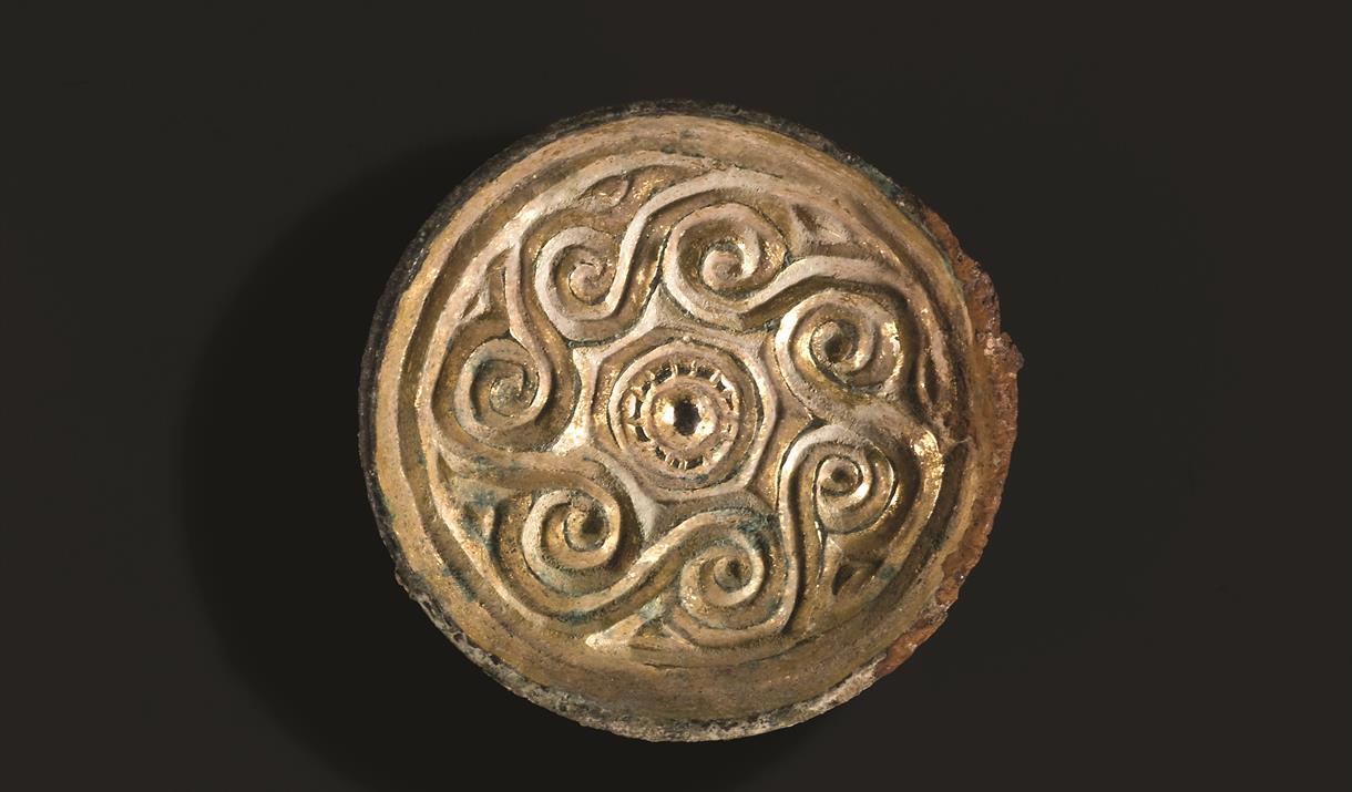 Shiny gold saucer brooch from Saxon Eastbourne with spiral decoration around edge