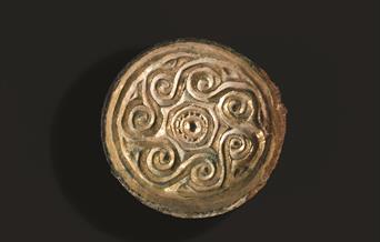 Shiny gold saucer brooch from Saxon Eastbourne with spiral decoration around edge