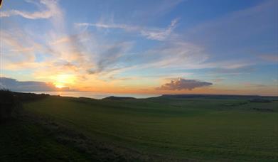 View from the back of the Beachy Head Story looking across a green field towards the sea at sunset
