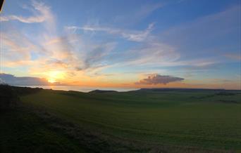 View from the back of the Beachy Head Story looking across a green field towards the sea at sunset