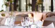Close up of an empty table set with white table cloth, wine glasses, cutlery and napkins