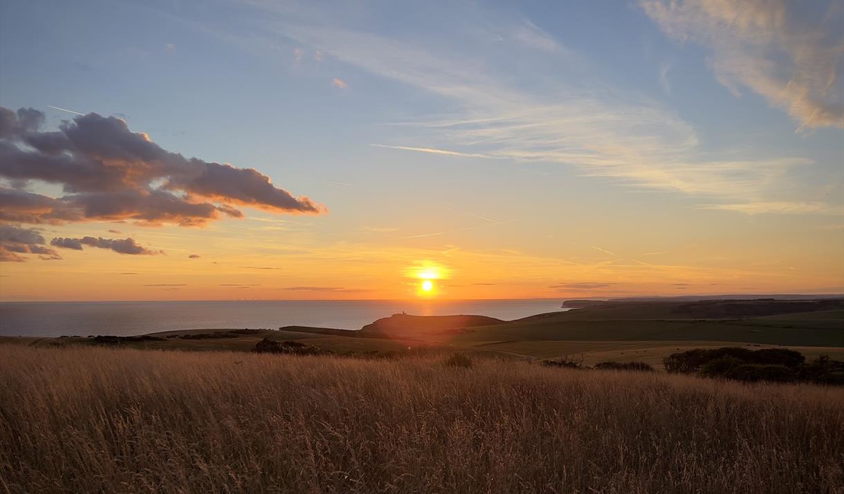 view across downland at sunset with belle tout lighthouse just visible beneath the setting sun