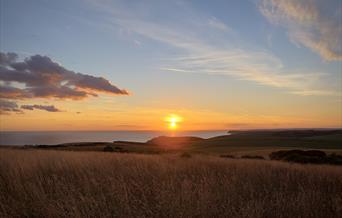 view across downland at sunset with belle tout lighthouse just visible beneath the setting sun