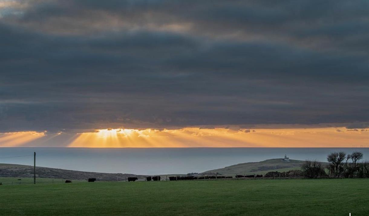 View of the Downland towards Belle Tout at Sunset - the sun's rays are just shining through a dark cloud