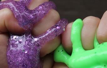 two children's hands holding purple and green slime