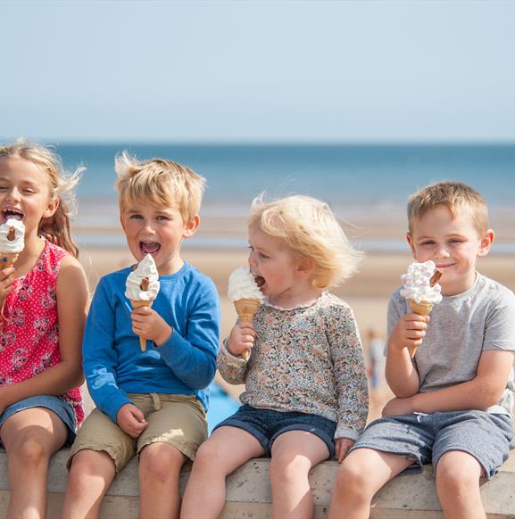 Children sitting on the promenade wall eating icecream in Bridlington in East Yorkshire.