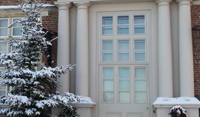 The entrance door, Christmas tree and wreaths, in the snow, at Burton Agnes Hall, East Yorkshire.