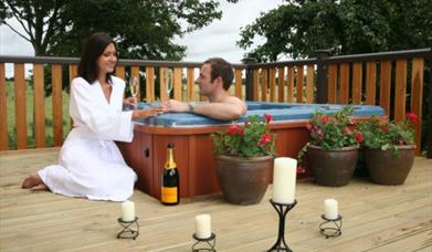 A couple enjoying a glass of champagne in a hot tub at Raywell Country Lodge Park in East Yorkshire.