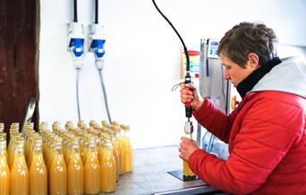 A lady filling bottles and the stock of bottles filled with apple juice at Yorkshire Wolds Apple Juice, in East Yorkshire