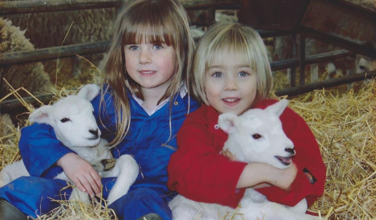 Two children sat in hay, holding two little lambs at Monk Fryston Beef and Lamb, in East Yorkshire