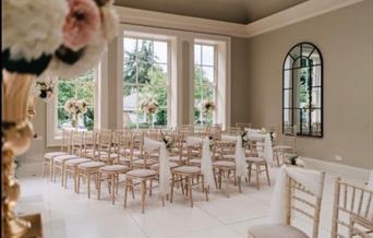 A room dressed for a wedding, complete with chairs and sashes, floral displays and large open windows/mirrors at Saltmarshe Hall, Goole in East Yorksh
