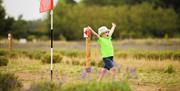 A young boy waving his arms in excitement next to a flag at wolds way lavender, in East Yorkshire