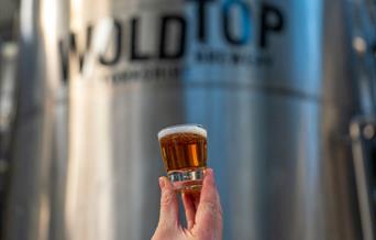 A person holding a glass of beer at Wold Top Brewery, Driffield in East Yorkshire.