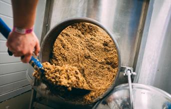 Someone scooping ingredients from a large drum at Atom Brewing Co, in East Yorkshire