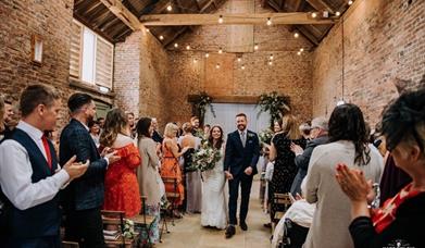 An image of a couple who have just got married at The Barns, with guests cheering & clapping.