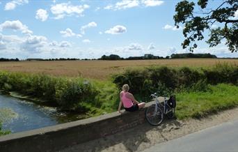 A woman sitting on a bridge, enjoying the view, with her bike leant against the bridge next to her, in East Yorkshire
